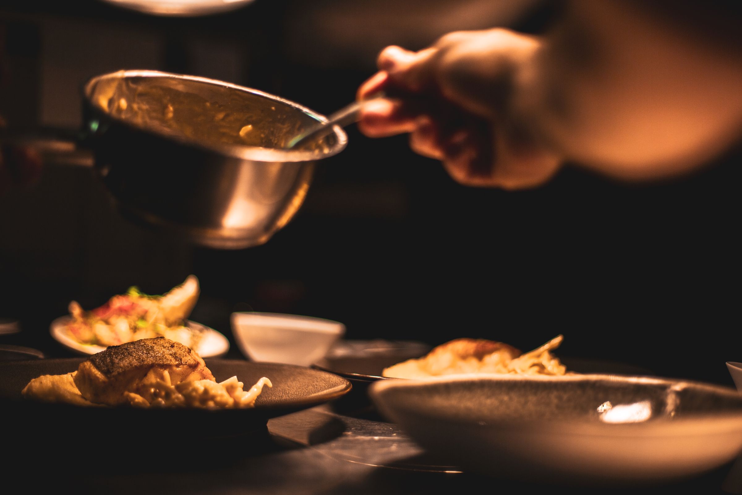 A sauce finished at the pass in a dark kitchen