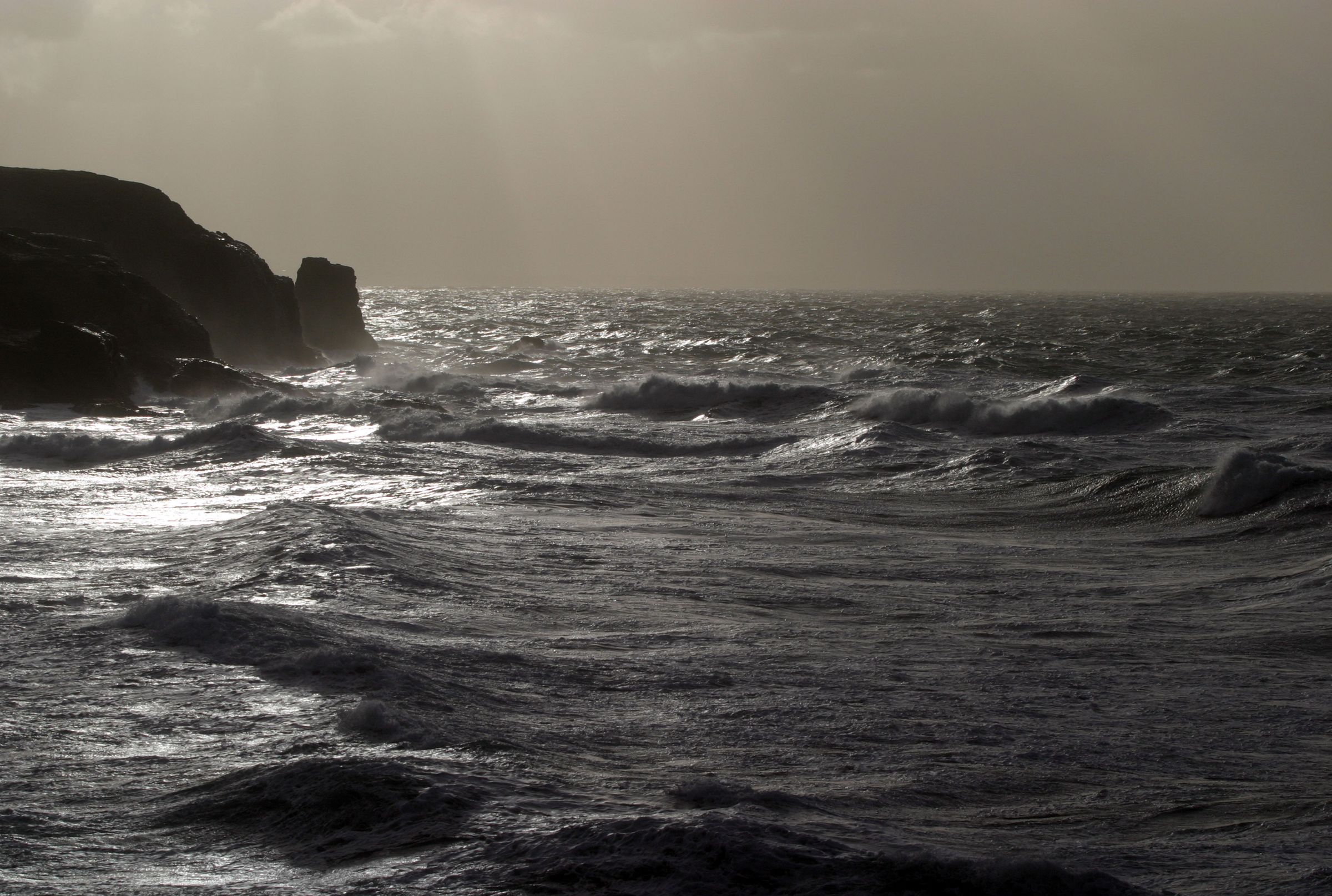 Storm light over a dark headland and running sea